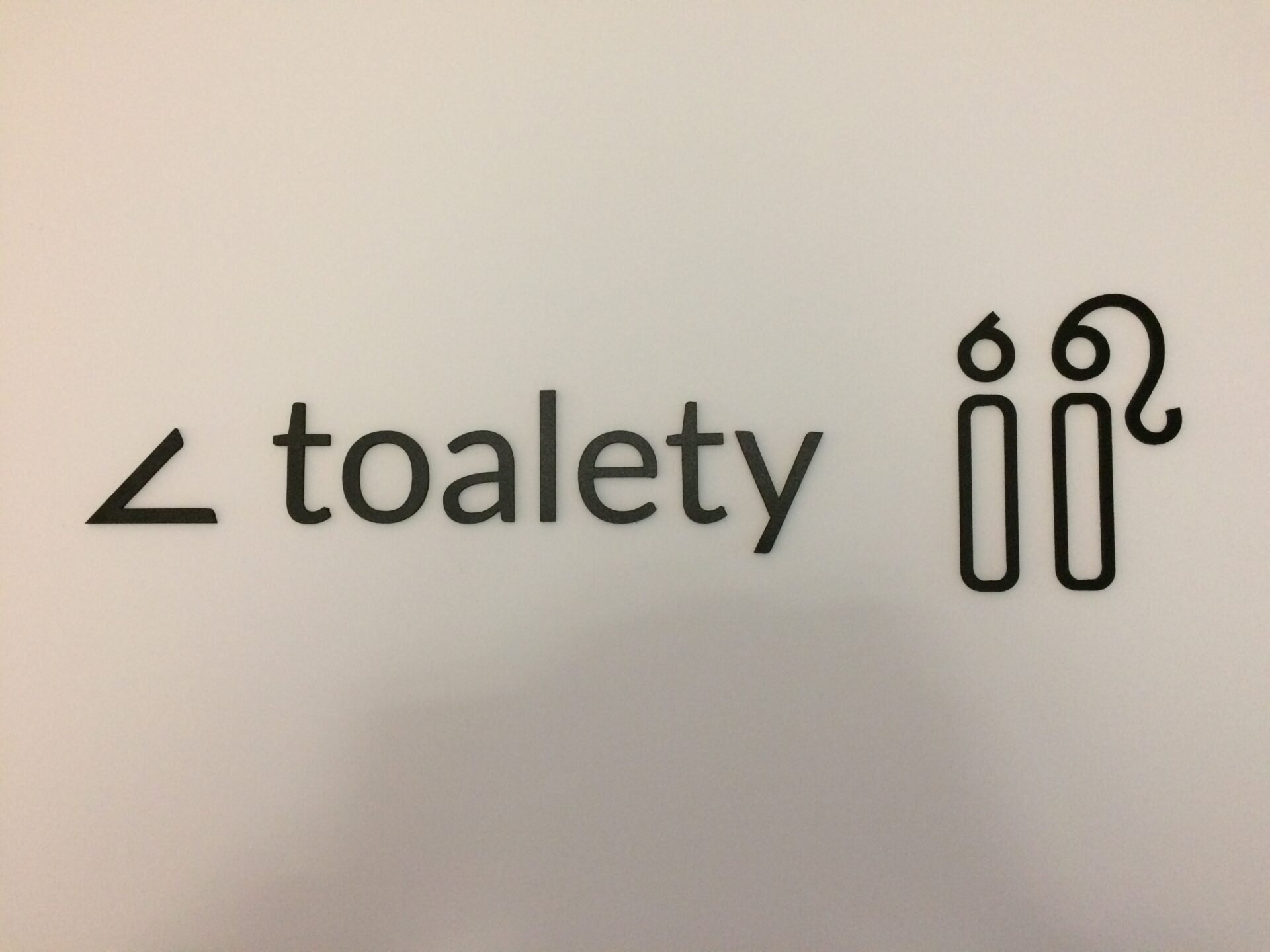 napis toalety z odpowiednimi piktogramami kobiety i mężczyzny oraz strzałką wskazującą kierunek w lewo