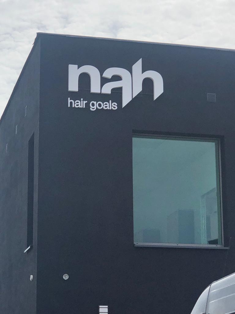 Białe podświetlane duże blokowe litery "nah hair goals" na zewnętrznej ścianie grafitowych budynków